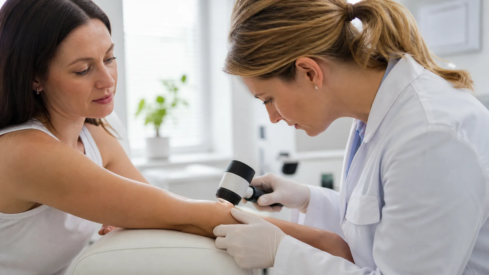 Dermatolog bada przedramię dorosłej osoby dermatoskopem podczas konsultacji.