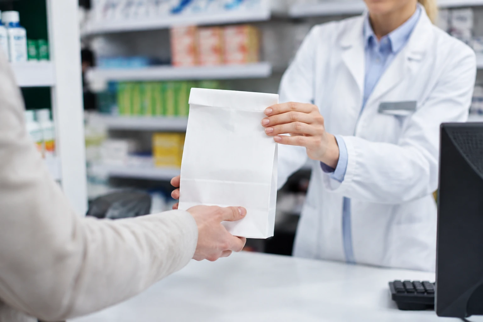 Farmaceuta przekazujący pacjentowi papierową torbę w aptece